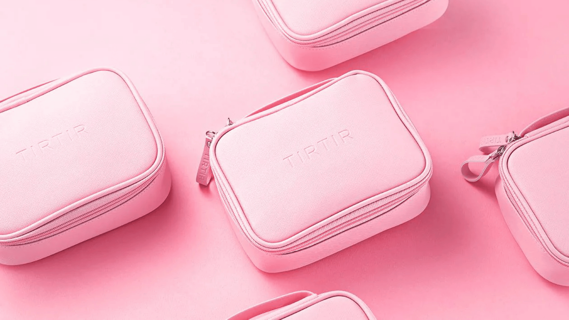 Bilden visar flera ljusrosa sminkväskor från märket TIRTIR. Deras enhetliga färg och stilrena design framhävs mot en mjukt rosa bakgrund, vilket ger en mycket sofistikerad och minimalistisk presentation. 