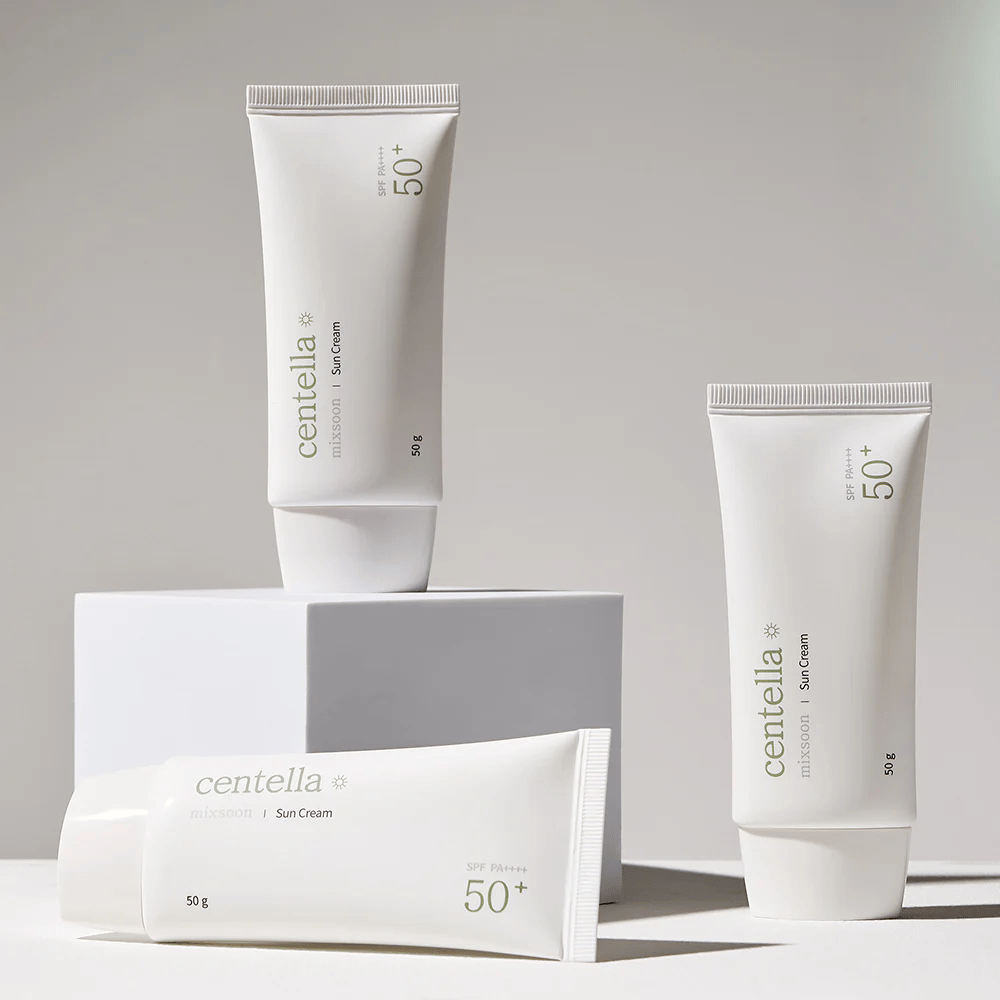 Tre förpackningar av Centella Sun Cream SPF 50+ PA++++ ordnade estetiskt på vita podier. Två tuber står upp och en ligger ner, alla med vita, minimalistiska design och gröna textdetaljer.