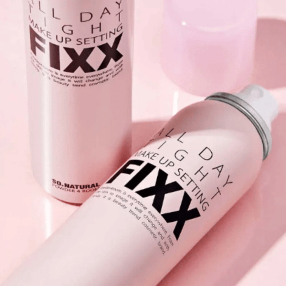 Två flaskor av So Natural All Day Tight Make Up Setting Fixx-spray, liggande och stående, på en rosa yta.
