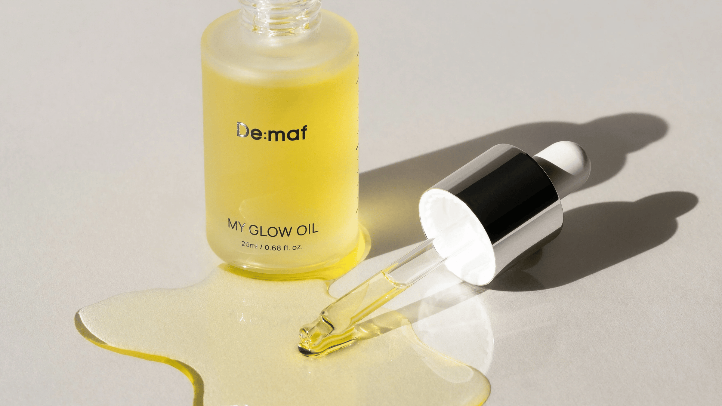 Produktbild av De:maf My Glow Oil som visar den gyllene ansiktsoljan i en frostad glasflaska tillsammans med en pipett fylld med olja.