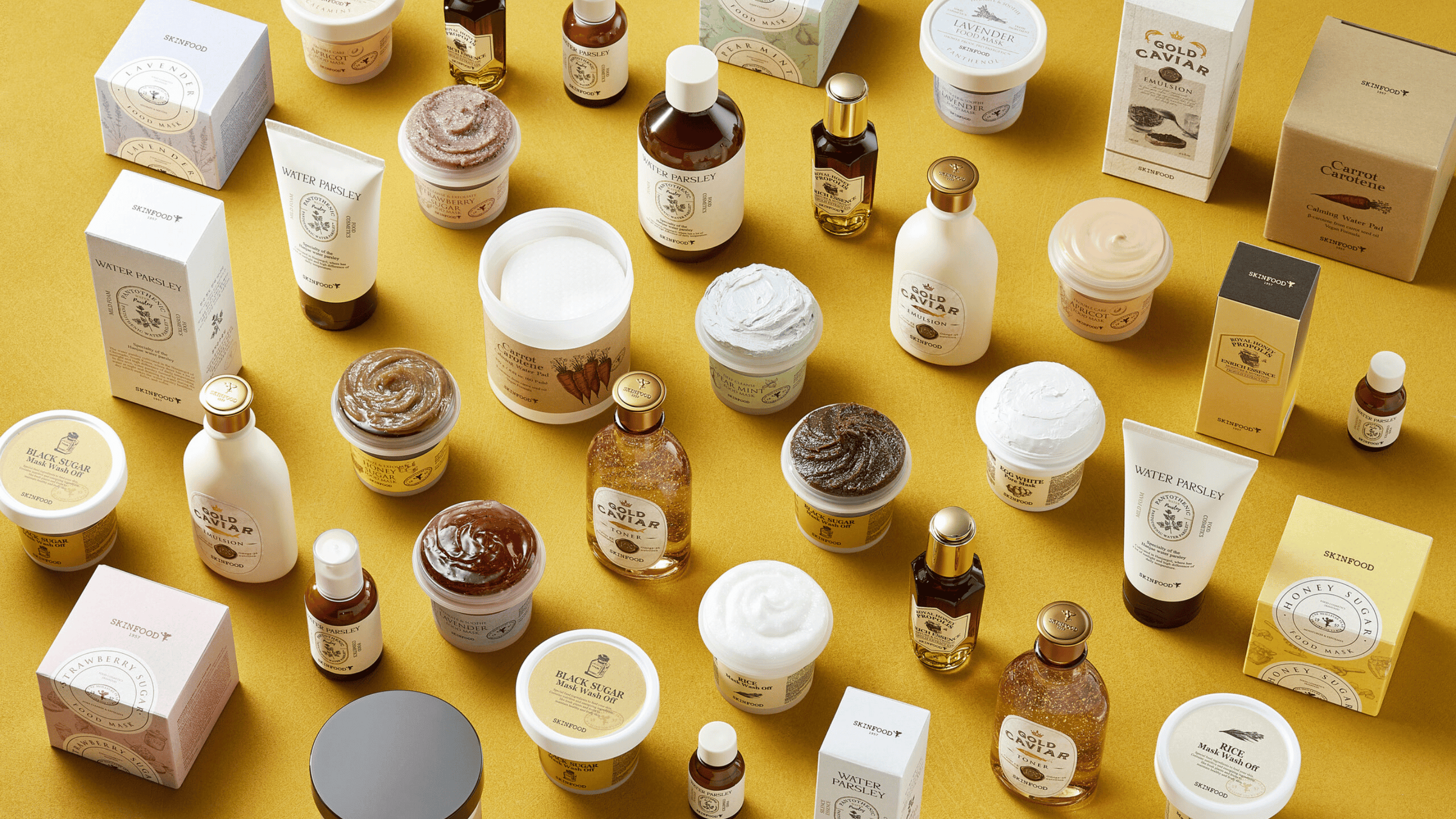 En samling av kosmetiska produkter från SKINFOOD på en gul bakgrund.