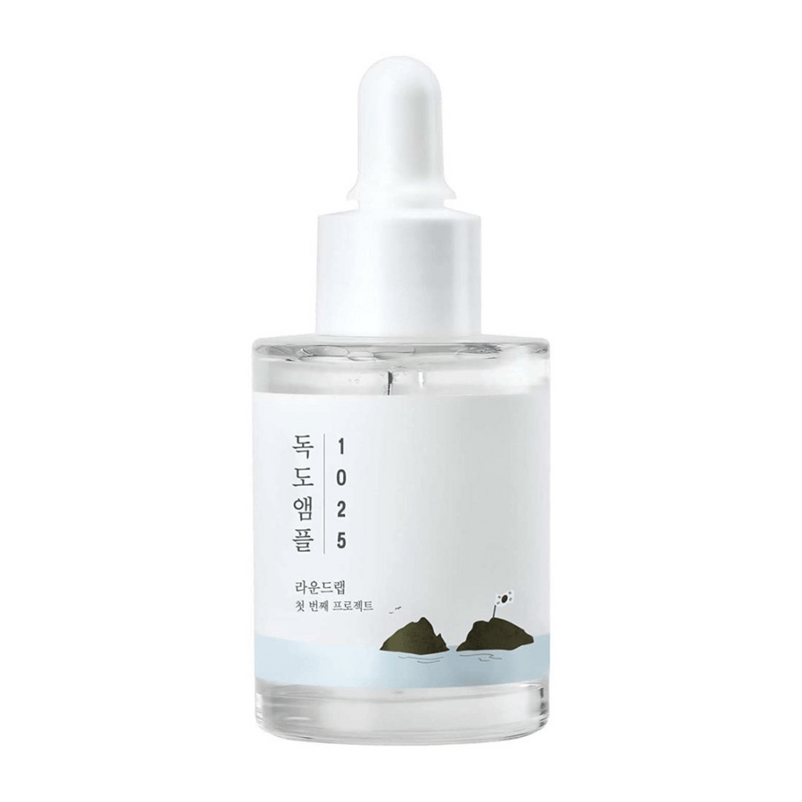 En genomskinlig flaska med 1025 Dokdo Ampoule ansiktsserum, dekorerad med minimalistiskt havstema, på vit bakgrund.