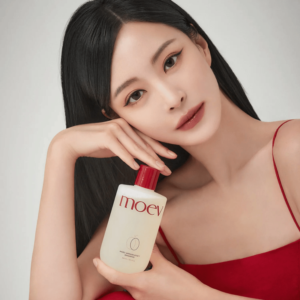 Kvinna med långt, glansigt hår håller MOEV Annurcatin Shampoo – ett koreanskt schampo som återfuktar, stärker och skyddar håret med naturliga ingredienser.