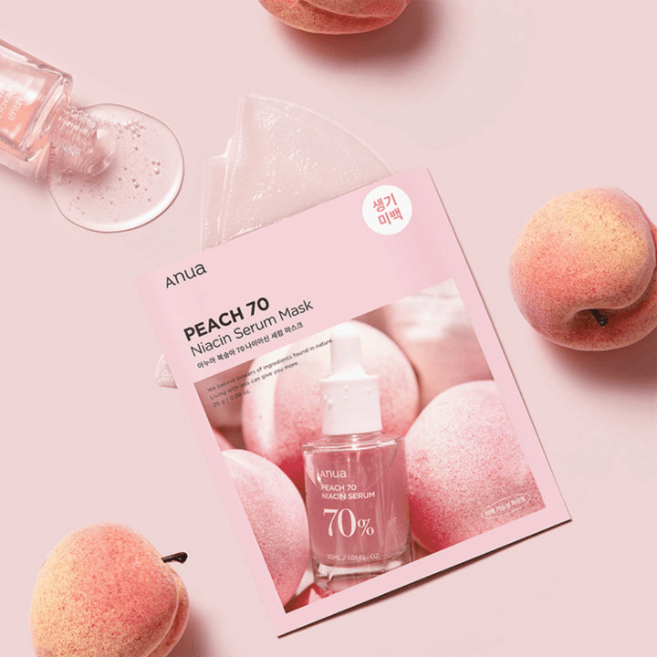 En bild av Anua PEACH 70 Niacin Serum Mask, omgiven av persikor och en flaska serum. Bilden har en mjuk rosa bakgrund, vilket kompletterar den rosa förpackningen och framhäver produkten och ingredienserna.