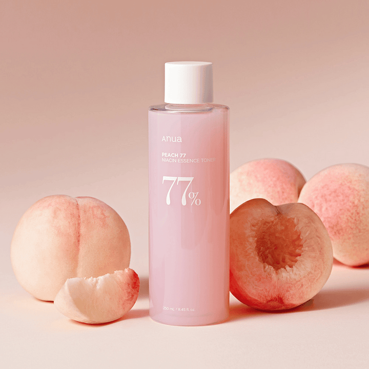 En flaska "Anua Peach 77 Niacin Essence Toner", omgiven av persikor.