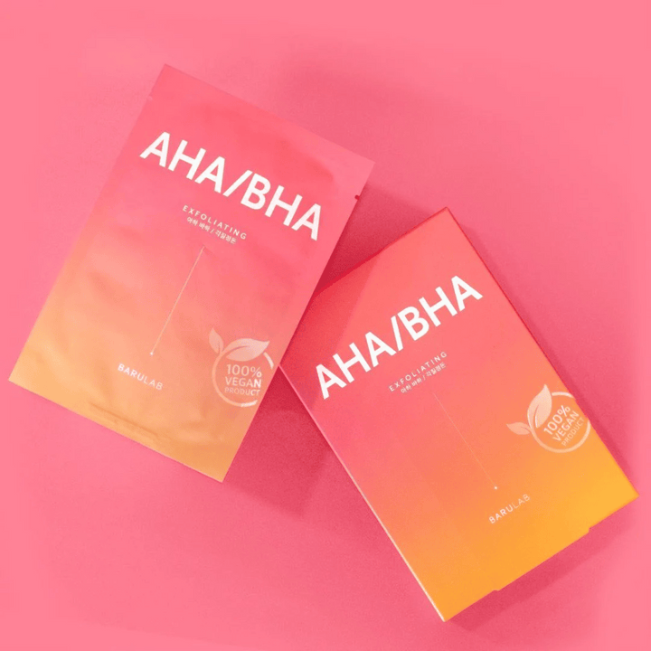 Två produkter från BARULAB, en i en påse och en i en kartong, båda  märkta med "AHA/BHA" och "Exfoliating" mot en rosa bakgrund. Produkterna är markerade som "100% Vegan Product".