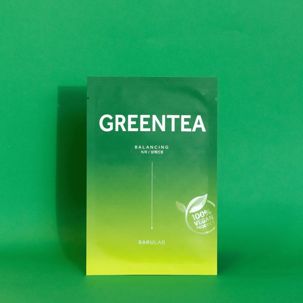 En förpackning från BARULAB för en "GREENTEA Balancing" mask, markerad som "100% Vegan Product". Förpackningens färg övergår från mörkgrönt upptill till ljusare grönt nertill, mot en enhetlig grön bakgrund.