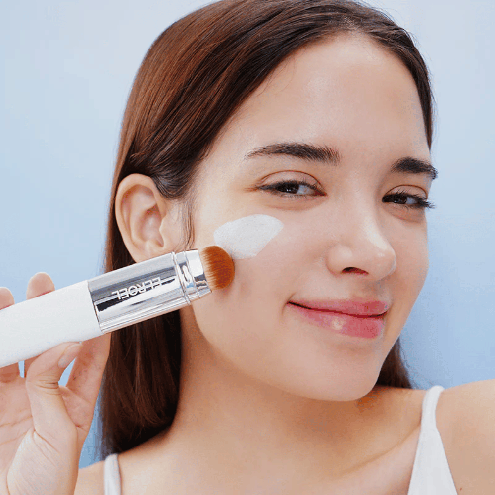 Modell applicerar ELROEL Blanc Cover Cream Stick concealer på kinden med inbyggd borste för naturlig och jämn täckning.