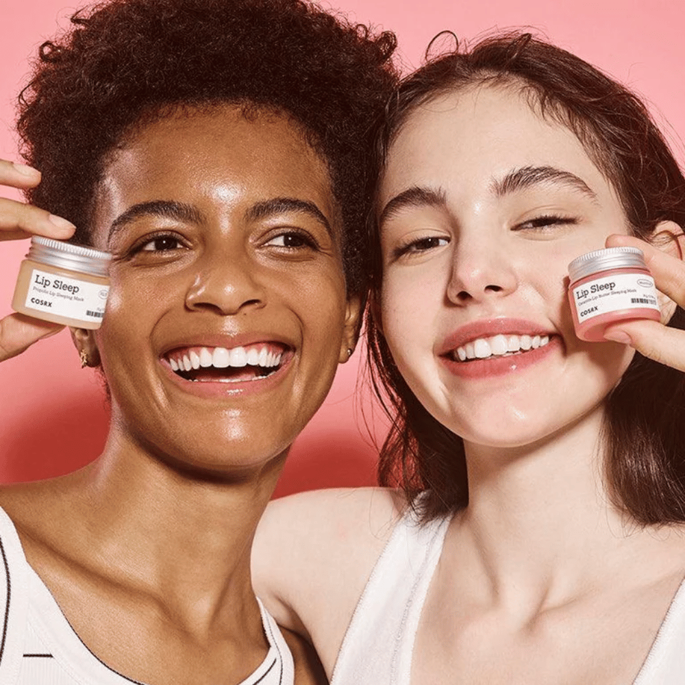Två personer ler och håller upp COSRX Lip Sleep-krukor. Bilden förmedlar mjuka, återfuktade läppar och produktens naturliga glödgivande effekt.