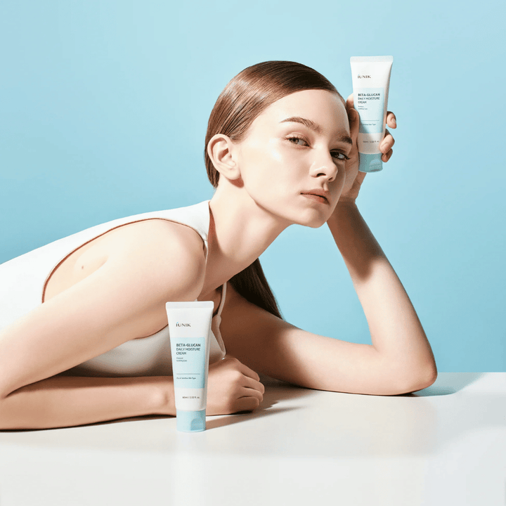 Livsstilsbild där en modell poserar med iUNIK Beta-Glucan Daily Moisture Cream mot en ljusblå bakgrund. Bilden förmedlar en ren, fräsch och återfuktande känsla samtidigt som produkten exponeras tydligt.