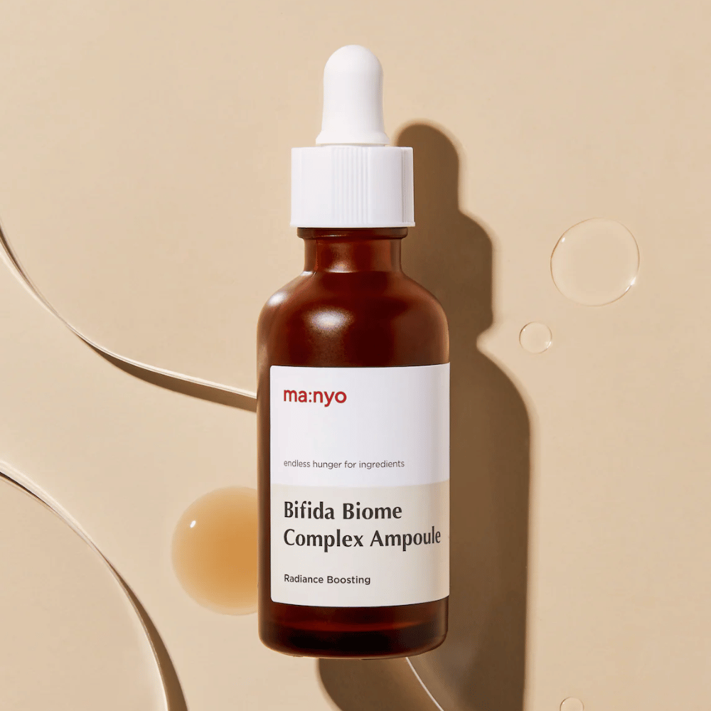 Stilren produktbild av ma:nyo Bifida Biome Complex Ampoule med fokus på flaskdesign och serumdroppar i bakgrunden.