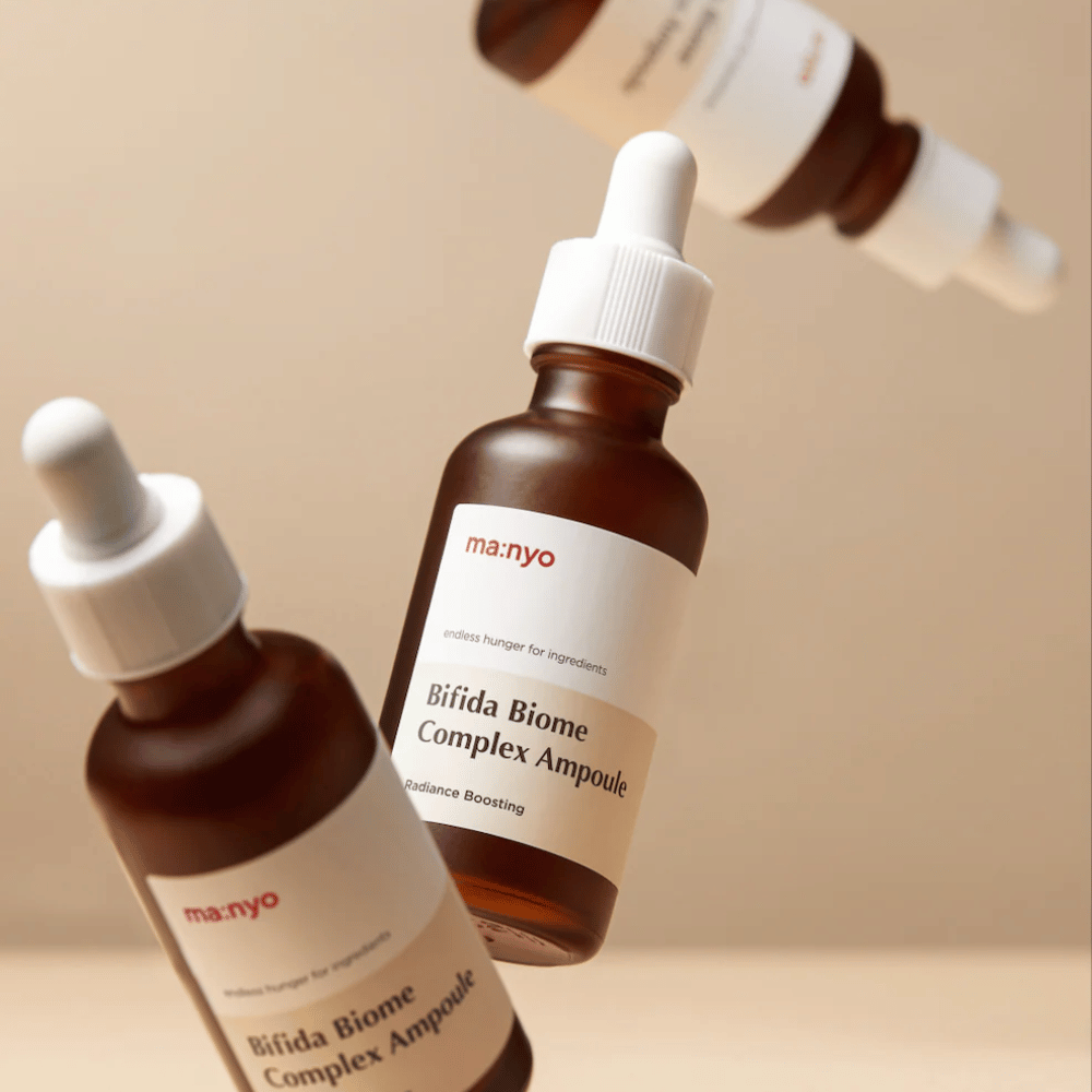 Produktbild med flera svävande flaskor av ma:nyo Bifida Biome Complex Ampoule mot beige bakgrund som ger en modern och minimalistisk känsla.