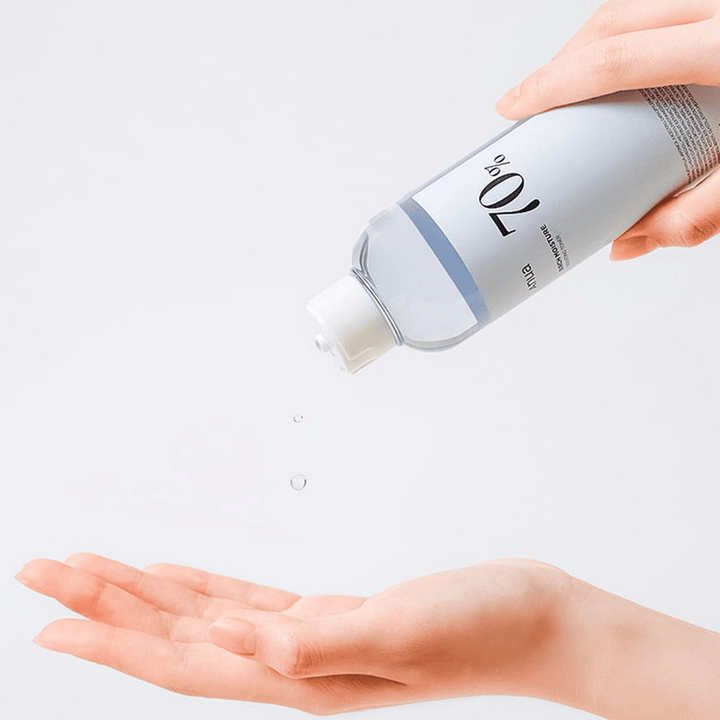 En flaska med Birch 70% Moisture Boosting Toner hålls lutad för att hälla ut produkten i en väntande hand mot en vit bakgrund.