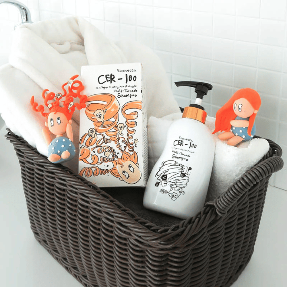 Presentationsbild med Elizavecca CER-100 Shampoo och produktförpackning placerade i en korg tillsammans med handdukar. Lekfulla figurer från förpackningsdesignen framhäver varumärkets unika och kreativa stil.