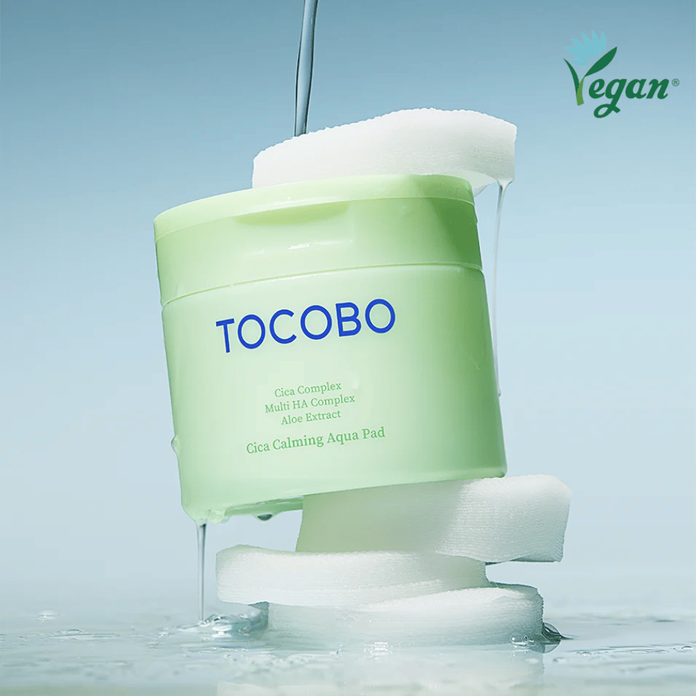 TOCOBO Cica Calming Aqua Pad placerad mellan toner pads med rinnande essence. Vegan-symbolen betonar produktens veganska formulering och hudvänliga profil.