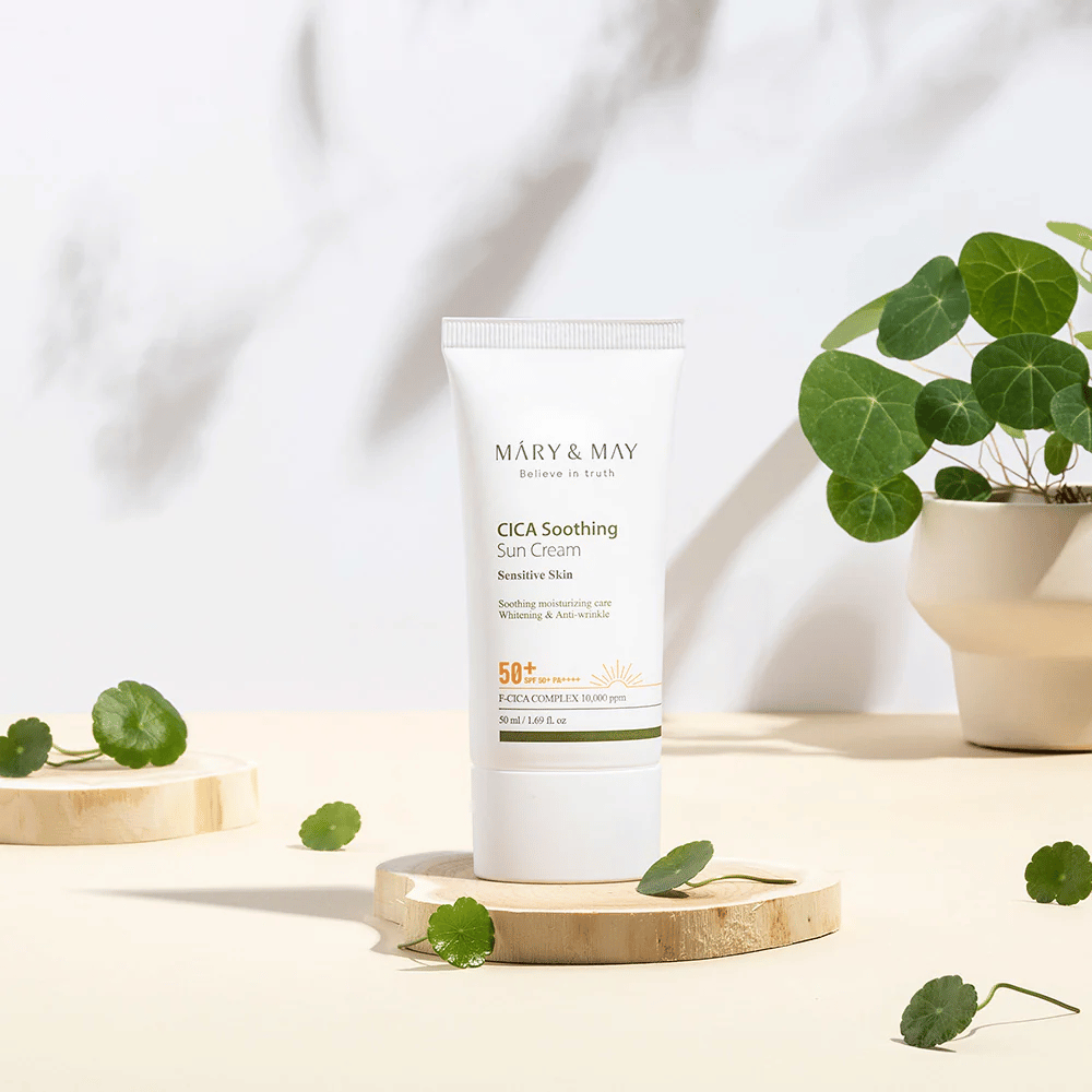 Mary&May CICA Soothing Sun Cream placerad på ett träpodium med gröna centella-blad runt omkring. Bilden betonar de hudlugnande ingredienserna och den naturliga inspirationen bakom produkten.