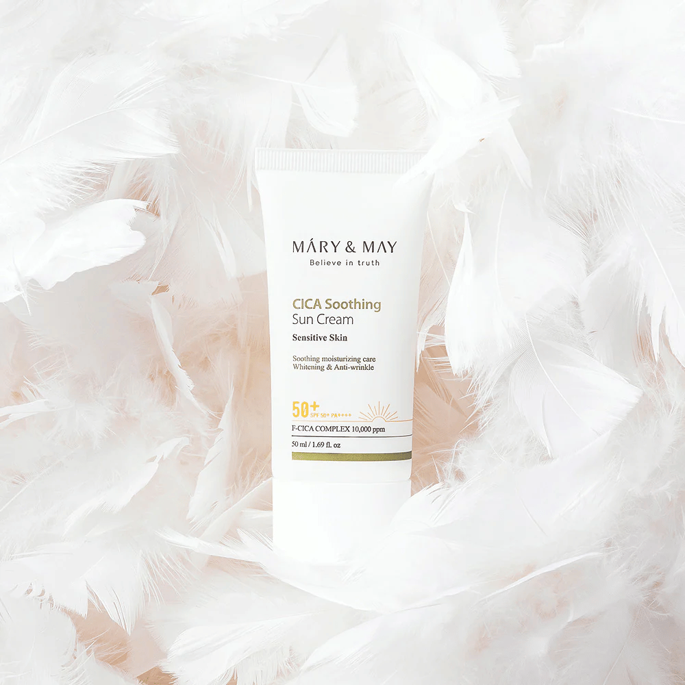 Mary&May CICA Soothing Sun Cream omgiven av mjuka vita fjädrar. Bilden förmedlar en känsla av skonsamhet, komfort och lätt formula anpassad för känslig hud.