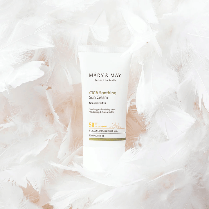 Mary&May CICA Soothing Sun Cream omgiven av mjuka vita fjädrar. Bilden förmedlar en känsla av skonsamhet, komfort och lätt formula anpassad för känslig hud.
