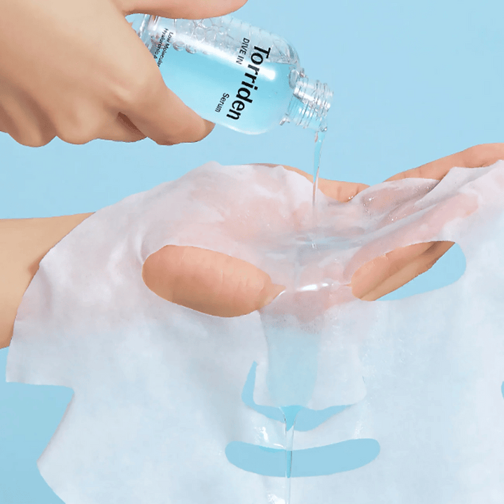 Ansiktsmask dränkt med lösning från en flaska "Torriden Dive-In", mot blå bakgrund.
