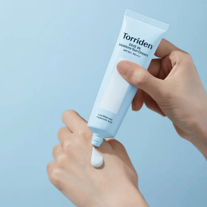 Torriden DIVE-IN Moisture Sun Cream SPF50+ PA++++ appliceras på handen för att visa den återfuktande solkrämens lätta och krämiga konsistens.
