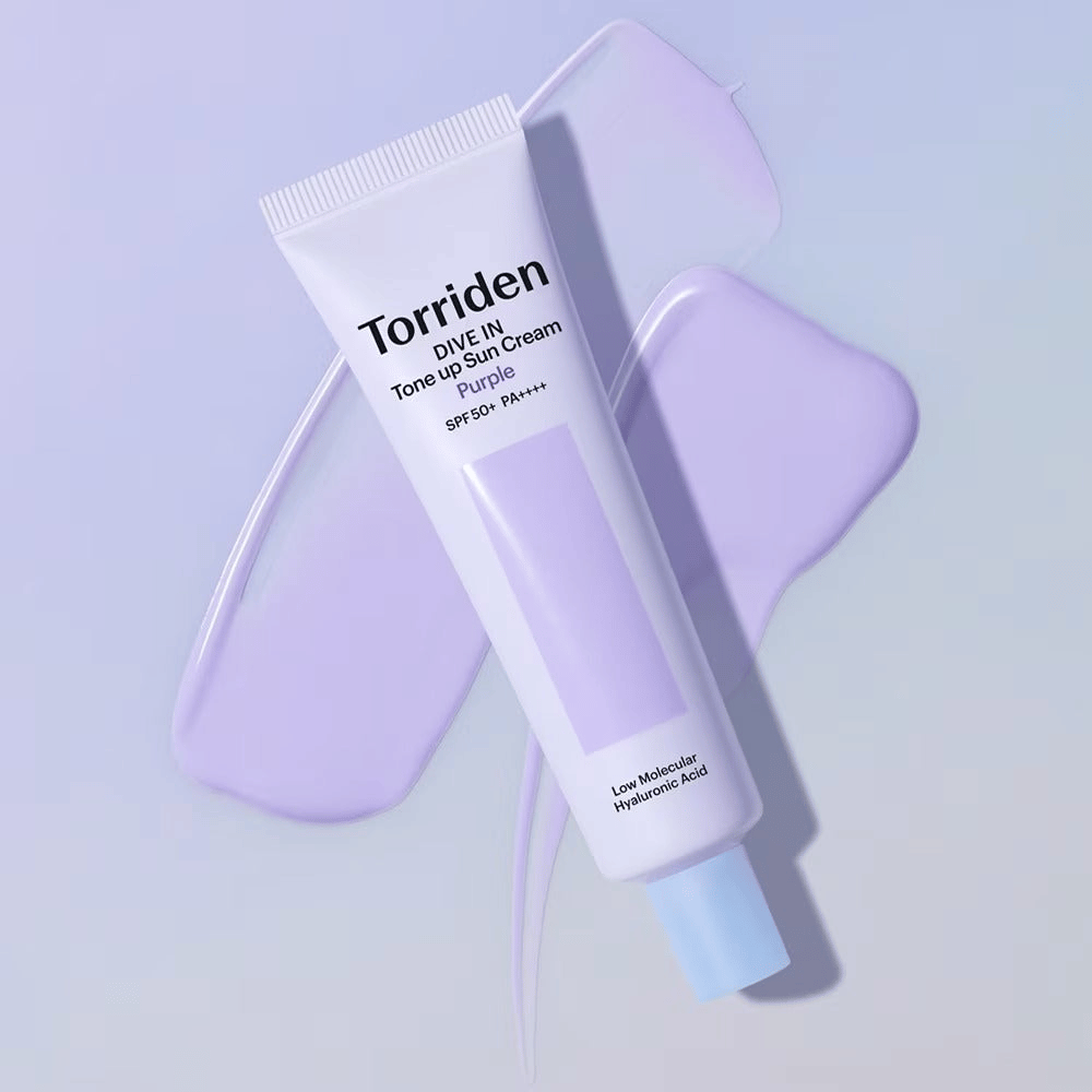 Torriden DIVE IN Tone Up Sun Cream Purple placerad på utsmetad lila kräm som framhäver den tonutjämnande och lystergivande effekten.