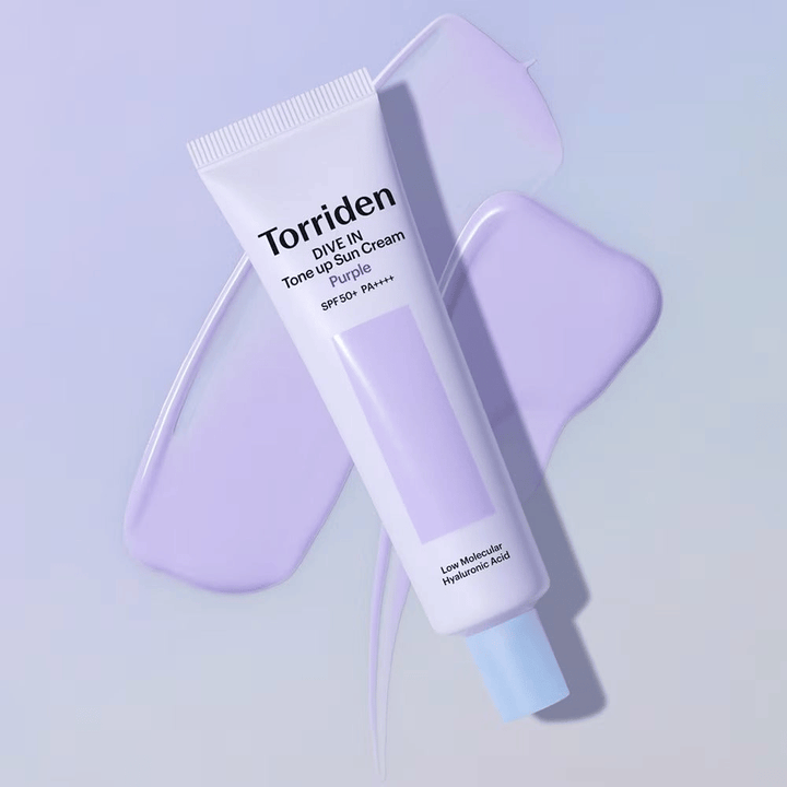 Torriden DIVE IN Tone Up Sun Cream Purple placerad på utsmetad lila kräm som framhäver den tonutjämnande och lystergivande effekten.