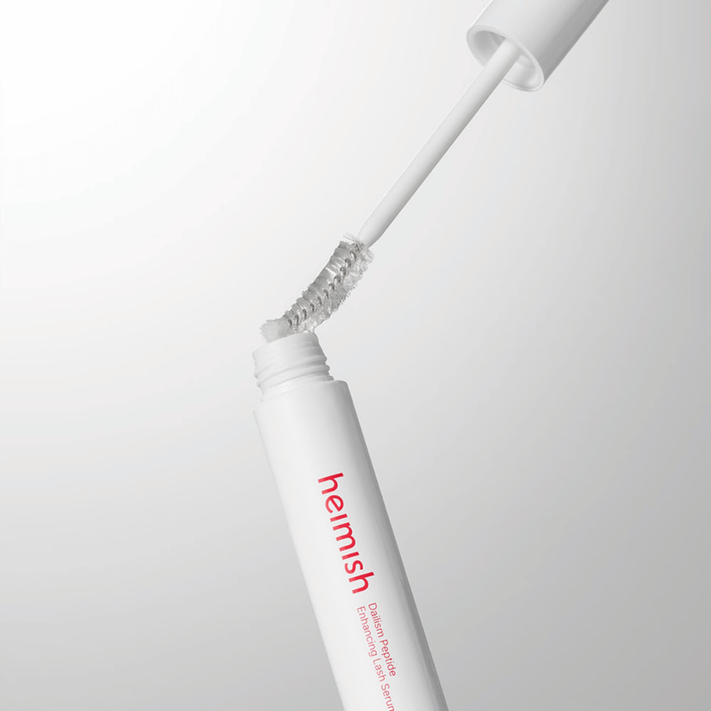 Närbild på applikatorn till Heimish Dailism Peptide Enhancing Lash Serum. Borsten dras upp ur den vita behållaren och visar den transparenta serumformulan som appliceras på fransarna.
