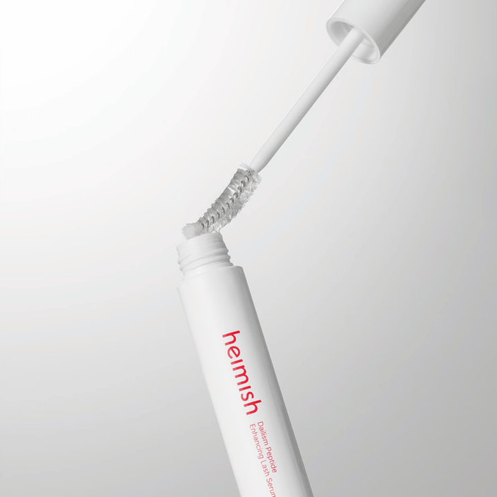 Närbild på applikatorn till Heimish Dailism Peptide Enhancing Lash Serum. Borsten dras upp ur den vita behållaren och visar den transparenta serumformulan som appliceras på fransarna.