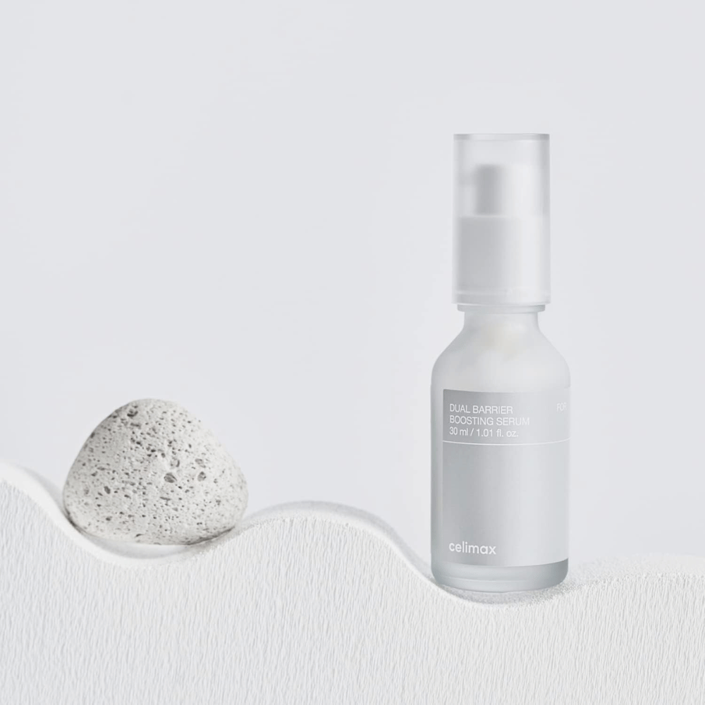 Celimax Dual Barrier Boosting Serum placerat på textil med sten, lugn produktbild som signalerar återfuktning och stärkt hudbarriär.