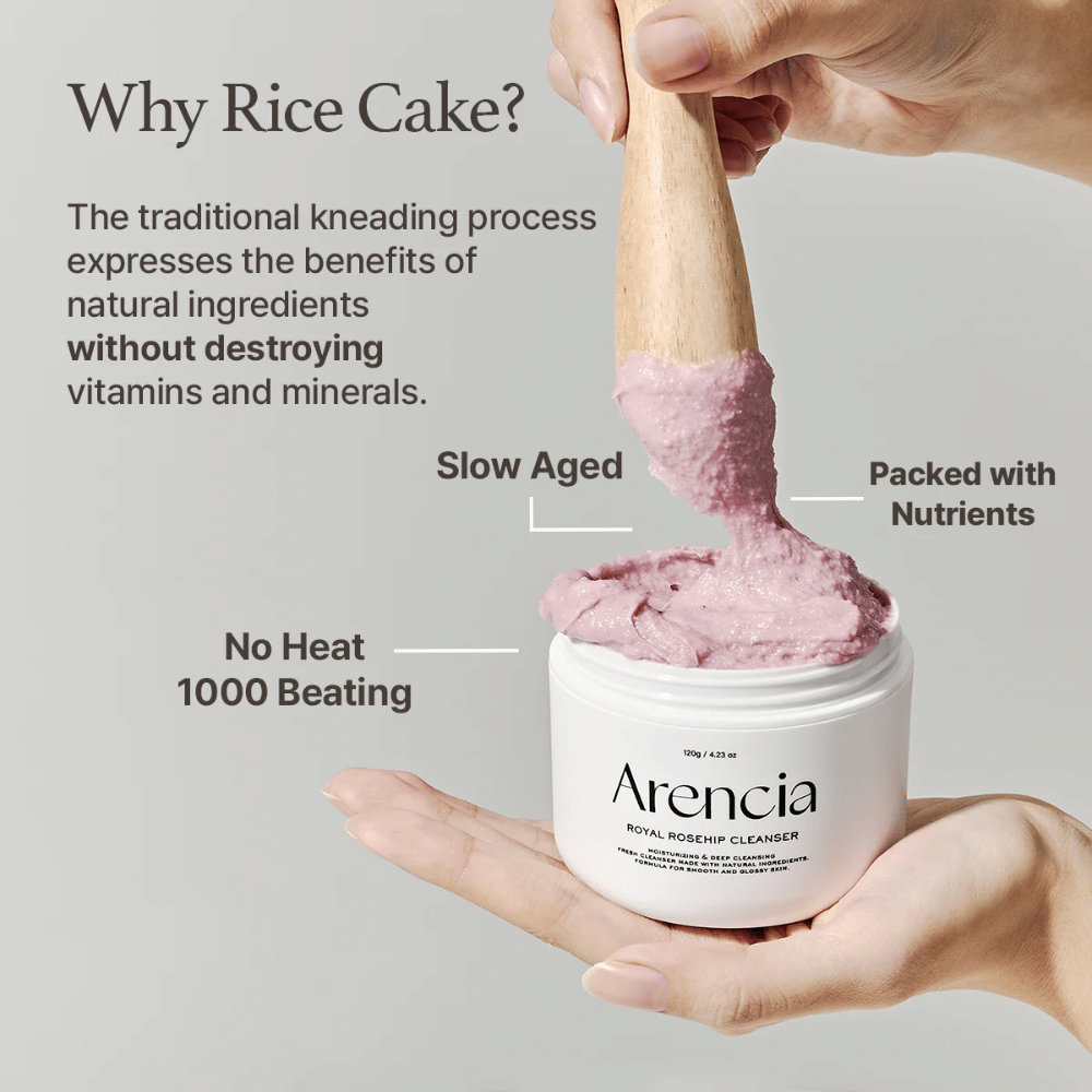 En hand håller i en öppen burk av Arencia Royal Rosehip Cleanser, med en rosa, mochi-liknande rengöringsformula som lyfts med en träspatel – visar produktens textur och traditionella tillverkningsmetod.