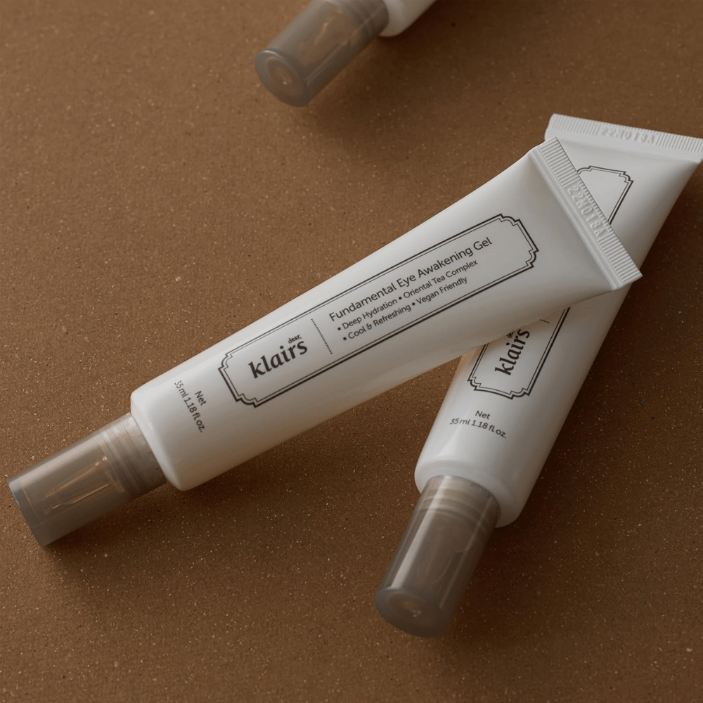 Lifestylebild med två tuber av Klairs Fundamental Eye Awakening Gel placerade mot en varm brun bakgrund. Kompositionen framhäver produktens eleganta design och premiumkänsla samtidigt som fokus ligger på ögonvård och återfuktning.