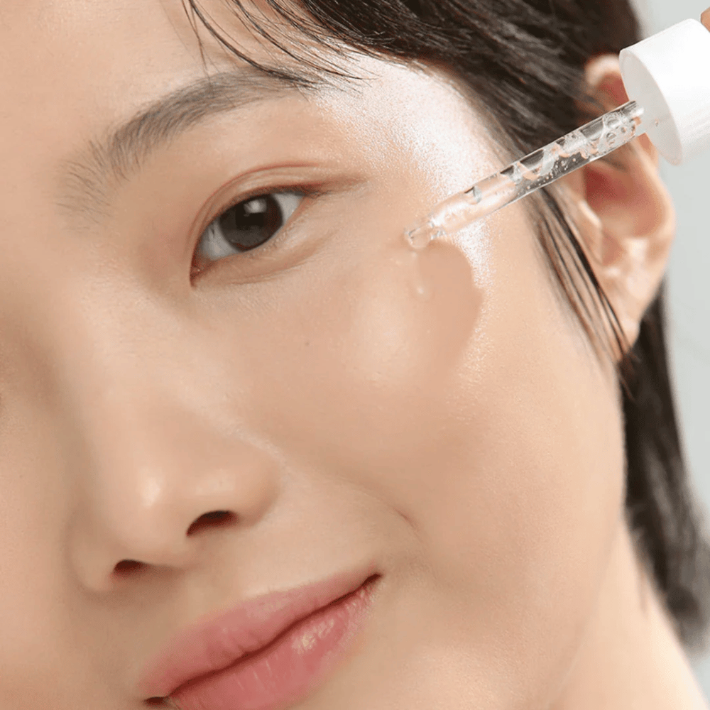 Närbild på kvinna som applicerar serum på kinden med pipett – hudvård som ger glow och återfuktning.