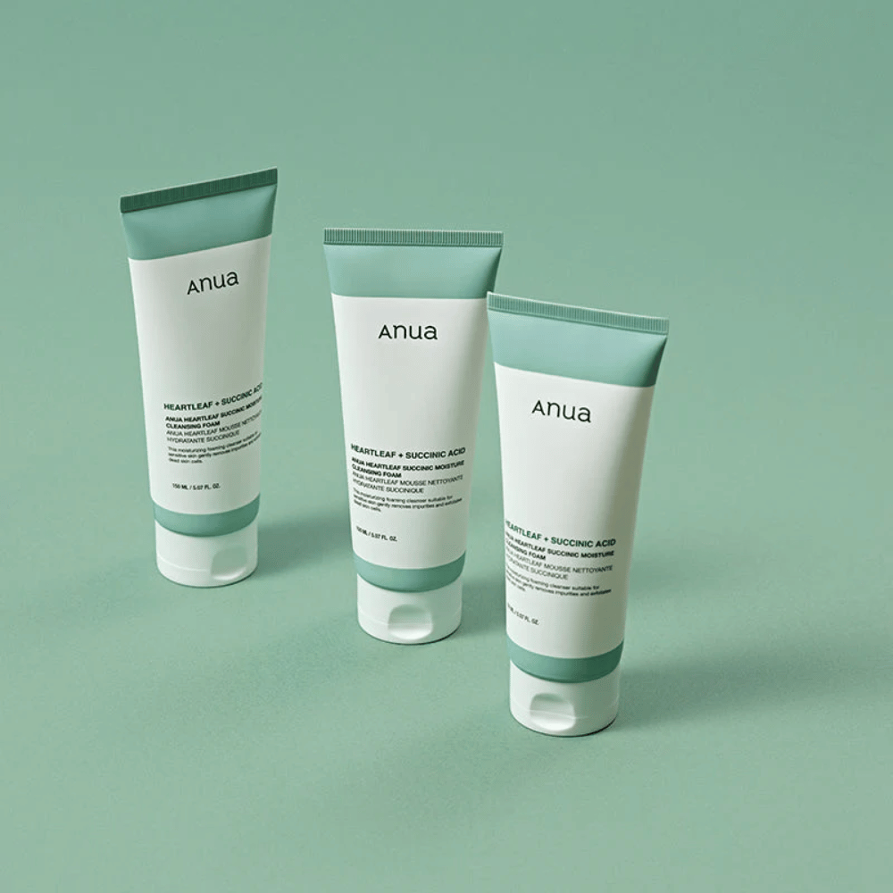 Tre förpackningar av Anua Heartleaf + Succinic Acid Moisture Cleansing Foam presenterade mot en ljusgrön bakgrund. Bilden framhäver produktens rena och minimalistiska design samt ger ett professionellt intryck av produktserien.