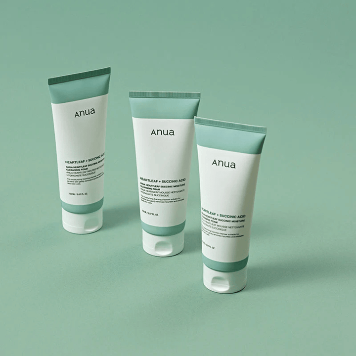 Tre förpackningar av Anua Heartleaf + Succinic Acid Moisture Cleansing Foam presenterade mot en ljusgrön bakgrund. Bilden framhäver produktens rena och minimalistiska design samt ger ett professionellt intryck av produktserien.