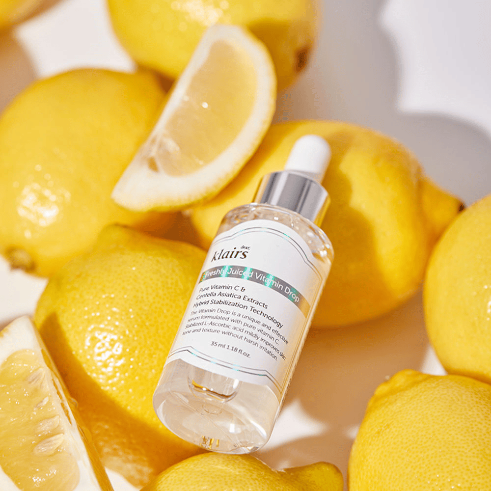 Klairs Freshly Juiced Vitamin Drop serumflaska omgiven av färska citronhalvor och citronskivor på en ljus yta, framhäver ingredienserna.