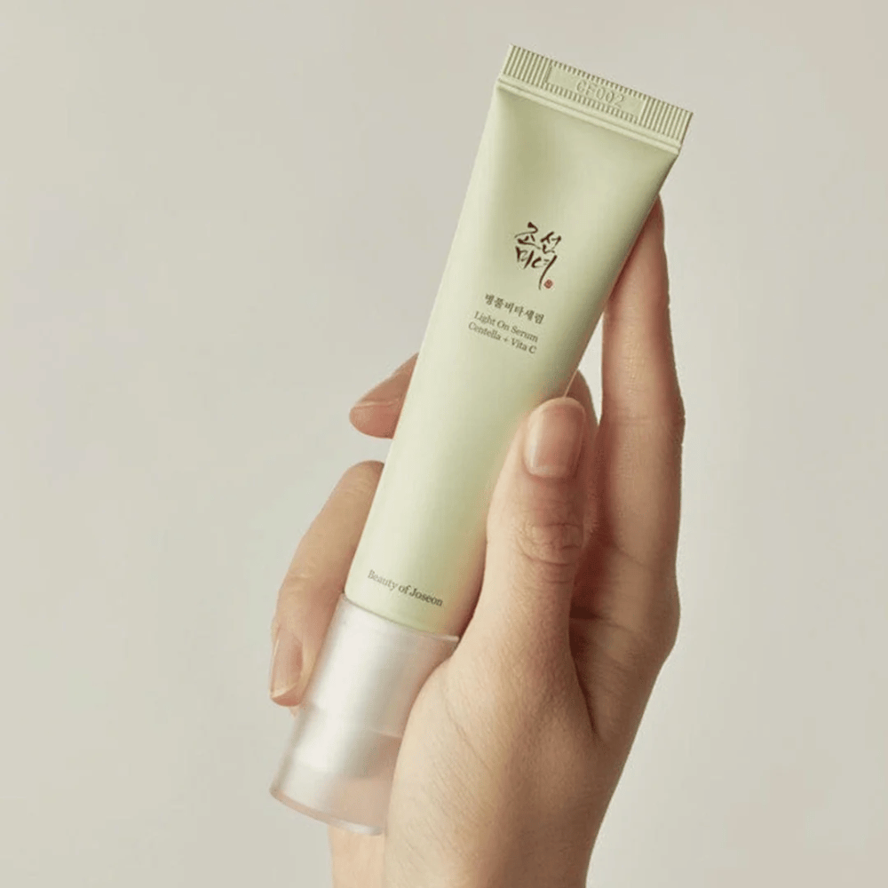 En hand håller i Beauty of Joseon Light On Serum med Centella och vitamin C, i en ljusgrön tub med minimalistisk design mot en neutral bakgrund.