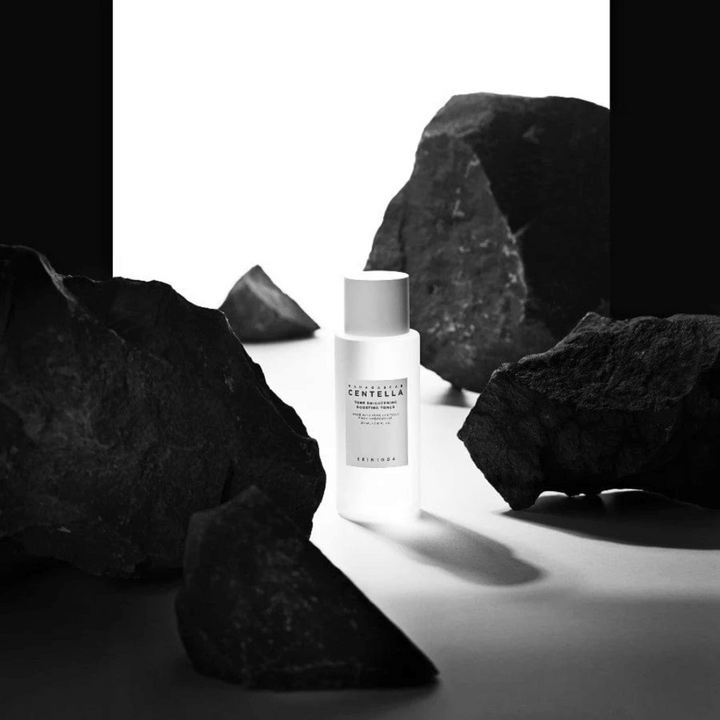 Vit flaska SKIN1004 Madagascar Centella Tone Brightening Boosting Toner placerad dramatiskt bland stora svarta stenar mot vit bakgrund.