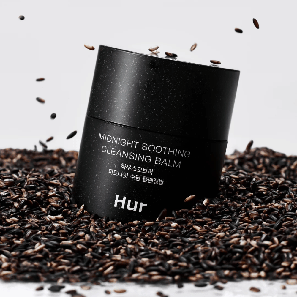 Hur Midnight Soothing Cleansing Balm i svart burk placerad på svarta frön. Lug­nande rengöringsbalm som löser makeup och orenheter samtidigt som huden vårdas.