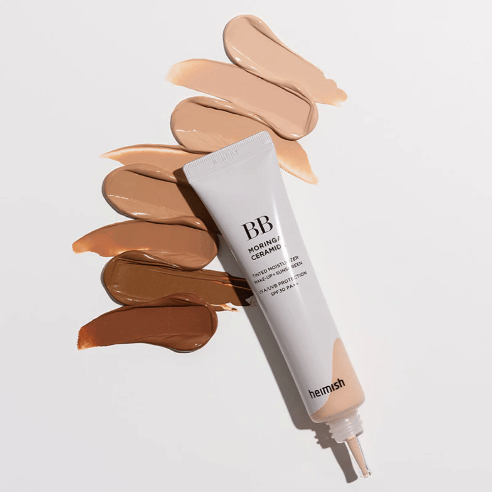 Heimish Moringa Ceramide BB Cream omgiven av flera nyansprover i olika hudtoner. Bilden visar produktens breda färgutbud och den krämiga konsistensen som ger naturlig täckning och jämn hudton.