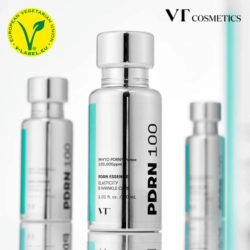 Flera silverfärgade flaskor av VT PDRN 100 Essence står uppradade, med tydlig märkning om 100,000 ppm PDRN och fokus på elasticitet och rynkvård. Överst syns logotypen för VT Cosmetics och ett V-label för vegetariskt innehåll.