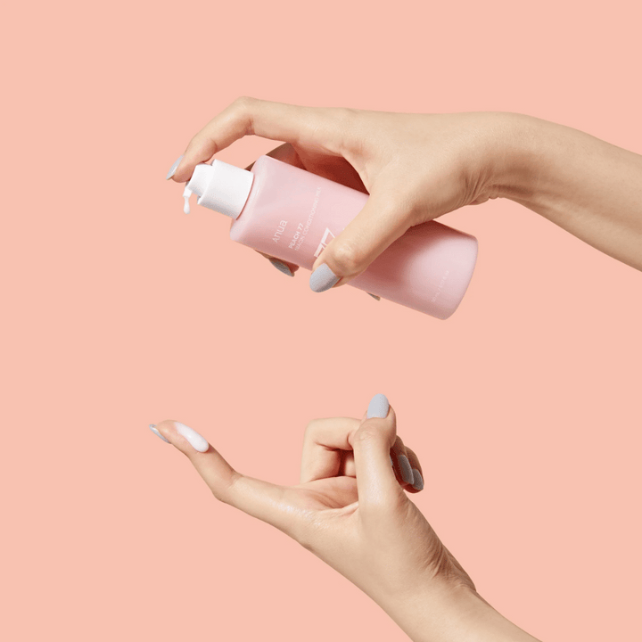 Bilden visar någons händer som håller en flaska med ANUA Peach 77% Niacin Conditioning Milk. Denna hudvårdsprodukt verkar ha en mjölkig konsistens och är designad för att vårda och förbättra hudens skick.
