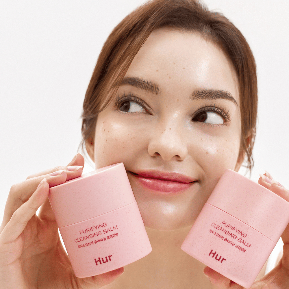Modell håller två burkar Hur Purifying Cleansing Balm. Mild rengöringsbalm som passar känslig hud och ger en fräsch, återfuktad känsla efter rengöring.