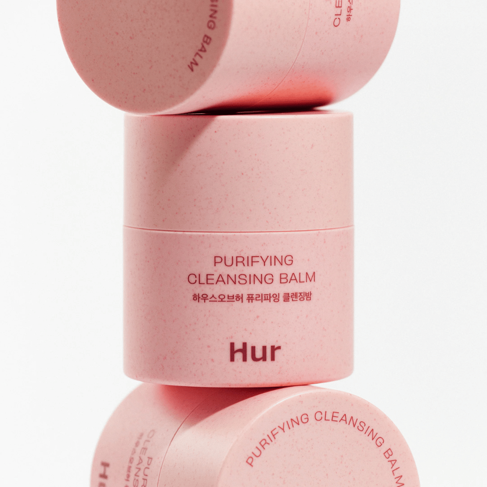 Hur Purifying Cleansing Balm i rosa förpackning staplad i studio. Rengörande cleansing balm som effektivt löser upp makeup, talg och orenheter utan att torka ut huden.