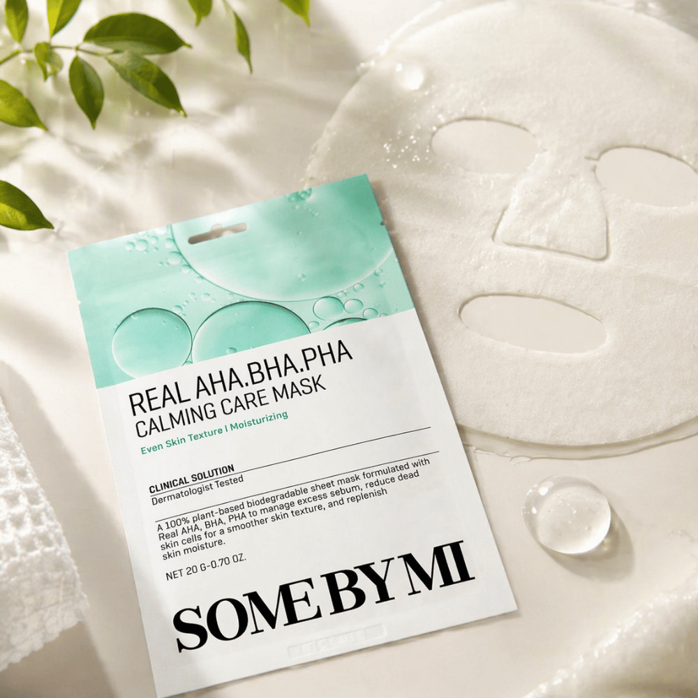 SOME BY MI Real AHA.BHA.PHA Calming Care Mask visas tillsammans med den utvecklade arkmasken. Runt produkten syns fuktdroppar och gröna blad som förstärker känslan av återfuktning, lugnande vård och skonsam exfoliering. Bilden lyfter fram maskens fokus på jämnare hudtextur och förbättrad fuktbalans.