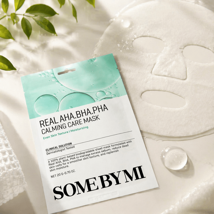 SOME BY MI Real AHA.BHA.PHA Calming Care Mask visas tillsammans med den utvecklade arkmasken. Runt produkten syns fuktdroppar och gröna blad som förstärker känslan av återfuktning, lugnande vård och skonsam exfoliering. Bilden lyfter fram maskens fokus på jämnare hudtextur och förbättrad fuktbalans.