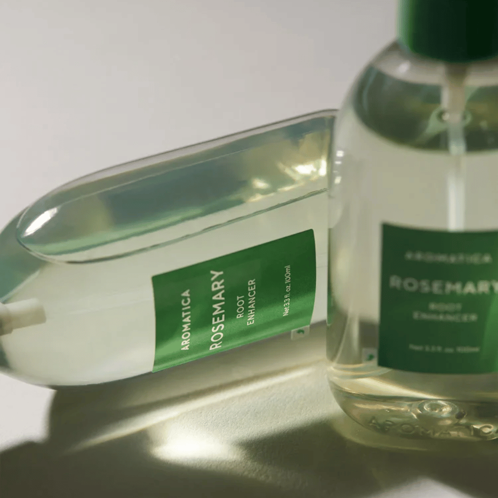 Två AROMATICA Rosemary Root Enhancer-flaskor med transparent skyddskåpa och grön etikett. Närbild som framhäver produktens premiumdesign och naturliga hårvårdskoncept.