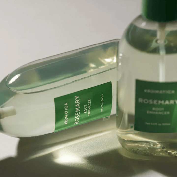 Två AROMATICA Rosemary Root Enhancer-flaskor med transparent skyddskåpa och grön etikett. Närbild som framhäver produktens premiumdesign och naturliga hårvårdskoncept.