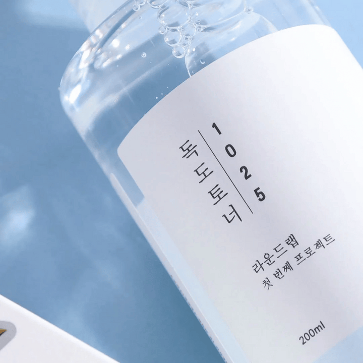 Närbild av en genomskinlig flaska Round Lab 1025 Dokdo Toner, fylld med klar vätska, mot en blå bakgrund.
