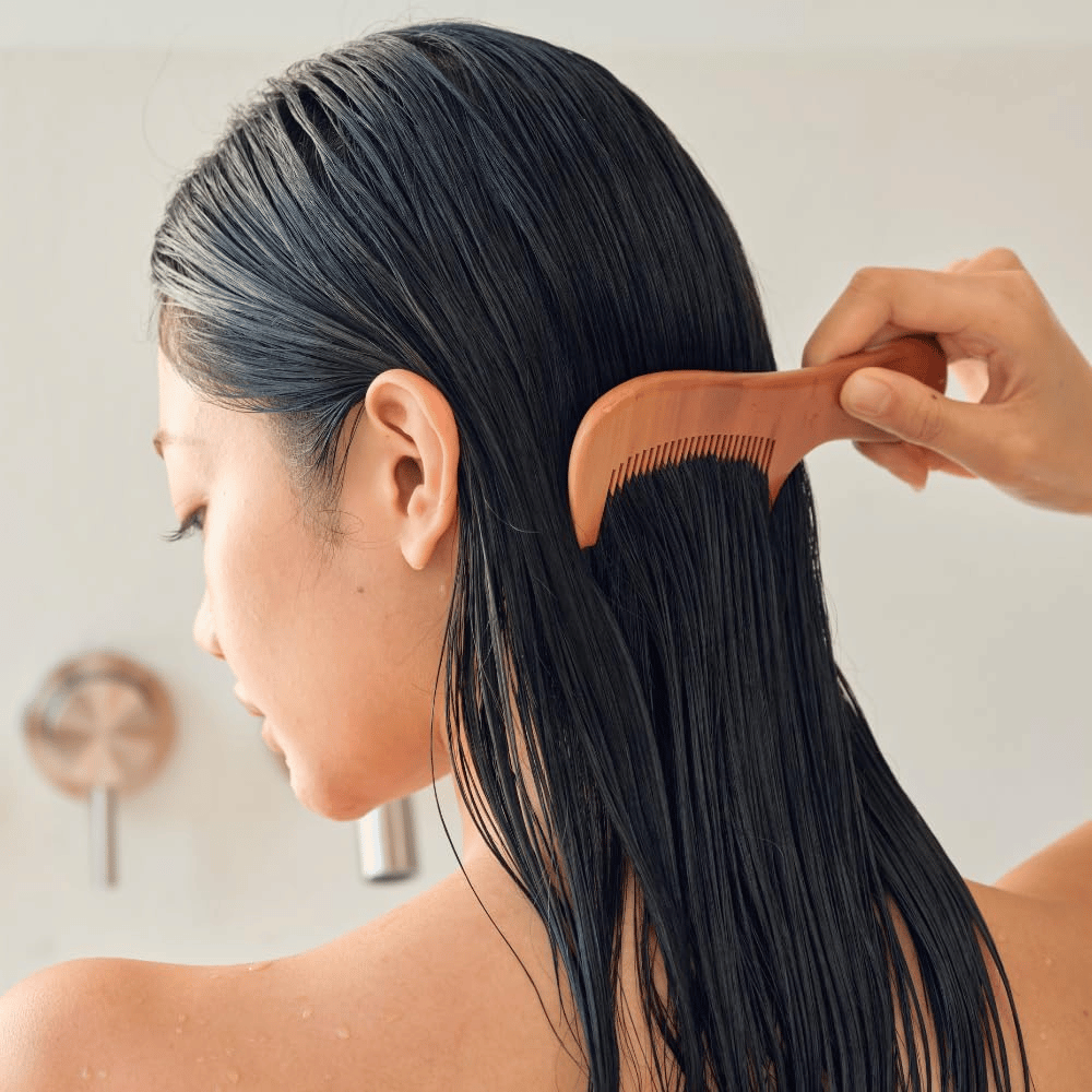 Person kammar igenom långt, vått hår med bred kam efter applicering av Heveblue Salmon Pullkeratin Centella Hair Treatment. Illustrerar utredande och mjukgörande effekt för ett slätare resultat.