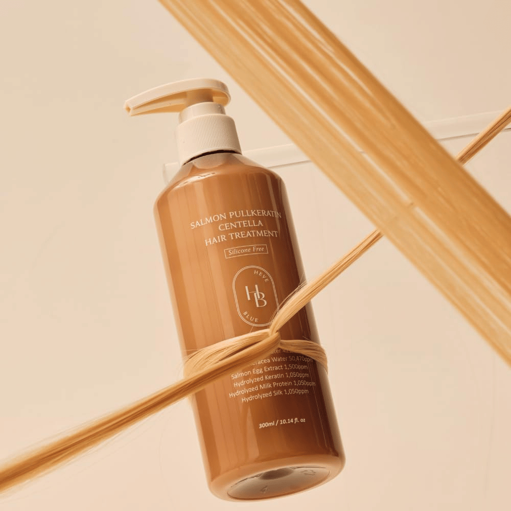 Heveblue Salmon Pullkeratin Centella Hair Treatment i brun flaska omgiven av hårslingor. Bilden lyfter fram hårbehandlingens vårdande egenskaper med fokus på glans, styrka och silkeslent hår.
